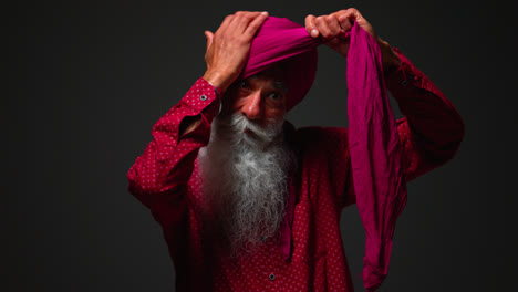 Low-Key-Studio-Lighting-Shot-Of-Senior-Sikh-Man-With-Beard-Tying-Fabric-For-Turban-Against-Dark-Background-Shot-In-Real-Time-2